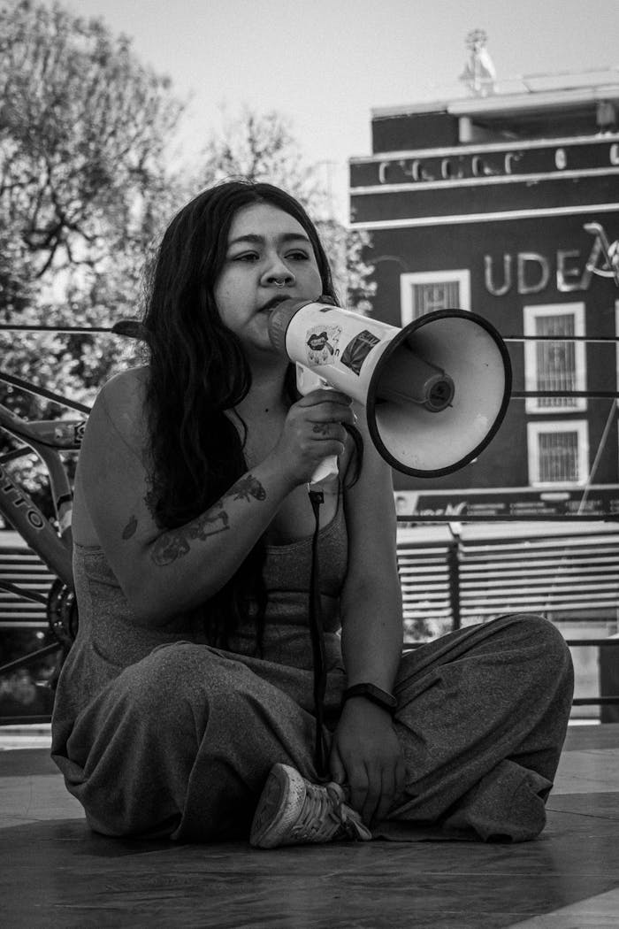 Black and white photo of a young woman with a megaphone, showcasing urban activism in a city setting.