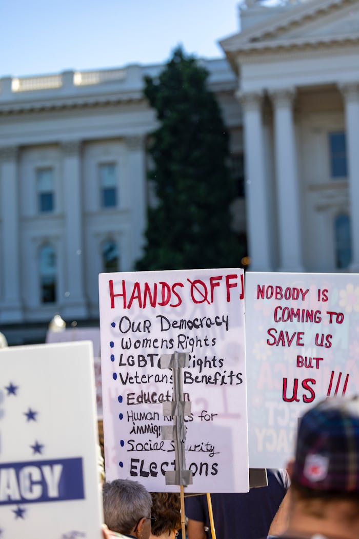 Protesters holding signs advocating for democracy, rights, and benefits outside the Sacramento Capitol.