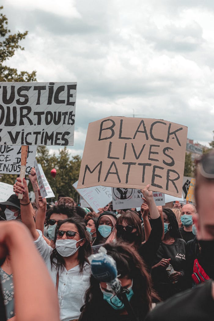 Crowd of diverse individuals at a Black Lives Matter protest holding signs and wearing masks.
